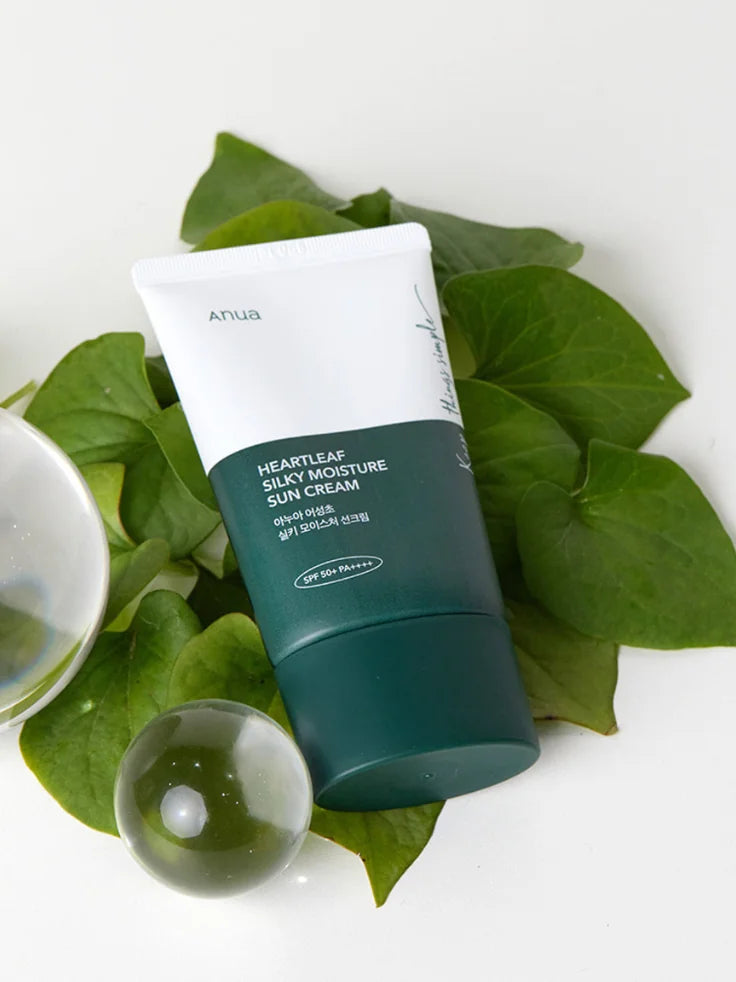 The ANUA Heartleaf Silky Moisture Sun Cream bottle next to fresh green heartleaf plants, emphasizing its key soothing ingredient.