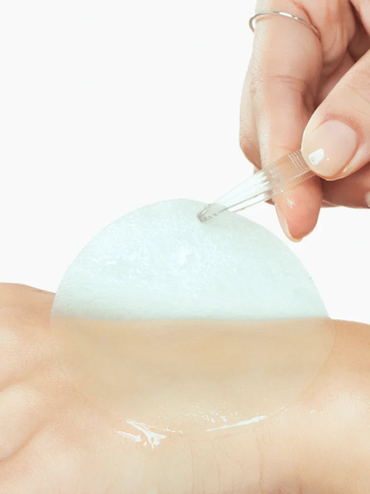 Close-up of one wet ANUA Glow Pad showing the dual sides: smooth gel side for a 5-minute hydration mask and textured side for gentle exfoliation.