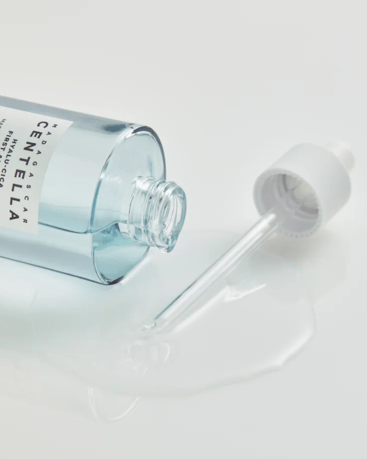 Close-up image of the Hyalu-Cica First Ampoule being dispensed by a dropper, emphasizing its watery, fast-absorbing texture. Centella Asiatica calming treatment.